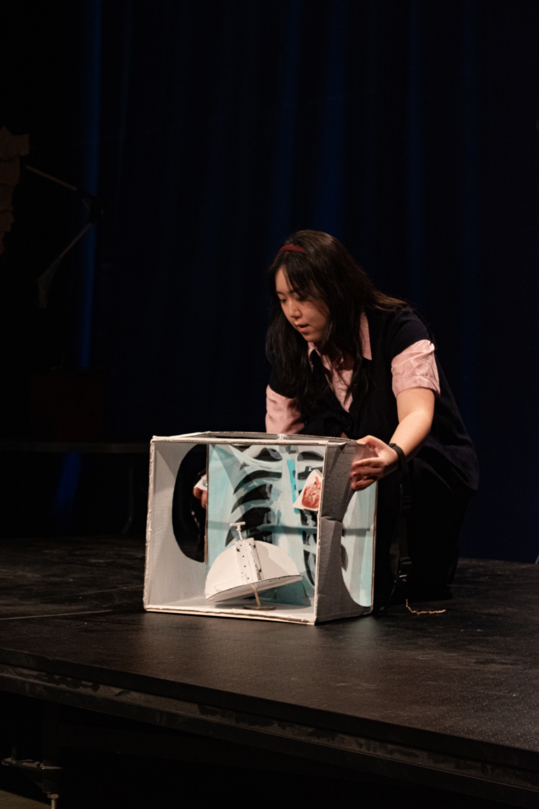 A student performer operating a handmade cardboard puppet theatre onstage